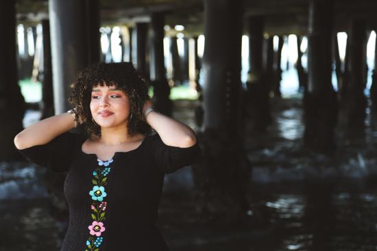 AJ posing and holding her hair under a pier at the beach